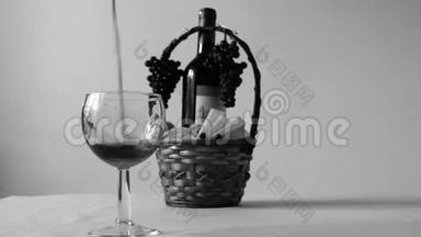 将红酒倒入玻璃杯中，粗糙。 一瓶红酒、葡萄和背景上有奶酪片的野餐篮